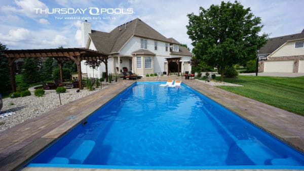Swimming pool with pergola on the side and house in the background.