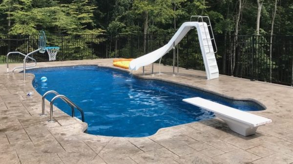 Swimming pool with pool slide, diving board, and pool basketball hoop.