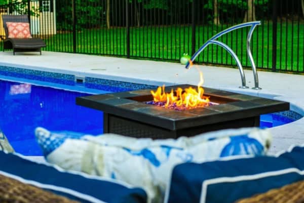 Fire pit with swimming pool and pool lounge chair in the background.