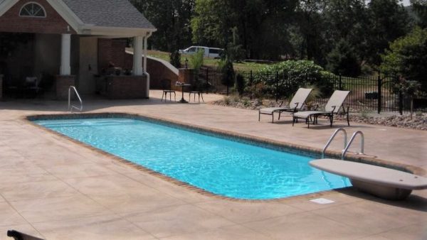Swimming pool with diving board, pool lounge chairs, and house in the background.