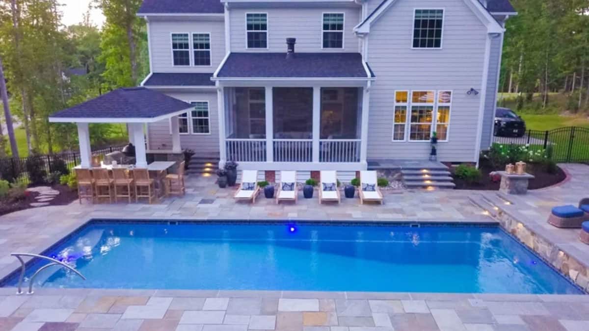 Swimming pool with pool lounge chairs, outdoor dinning set, and house in the background.