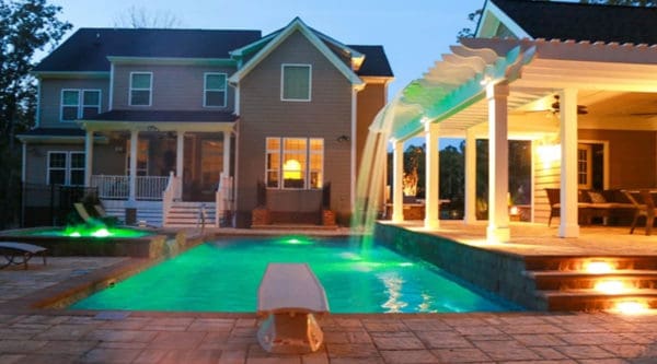 Swimming pool with integrated spa, pergola on the side, and house in the background.