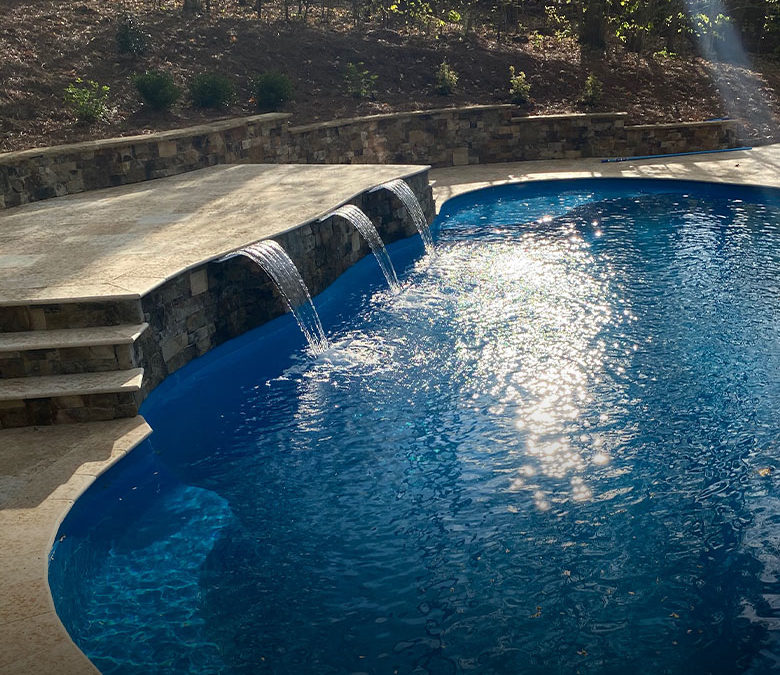 inground fiberglass pool with a waterfall ledge and retaining wall