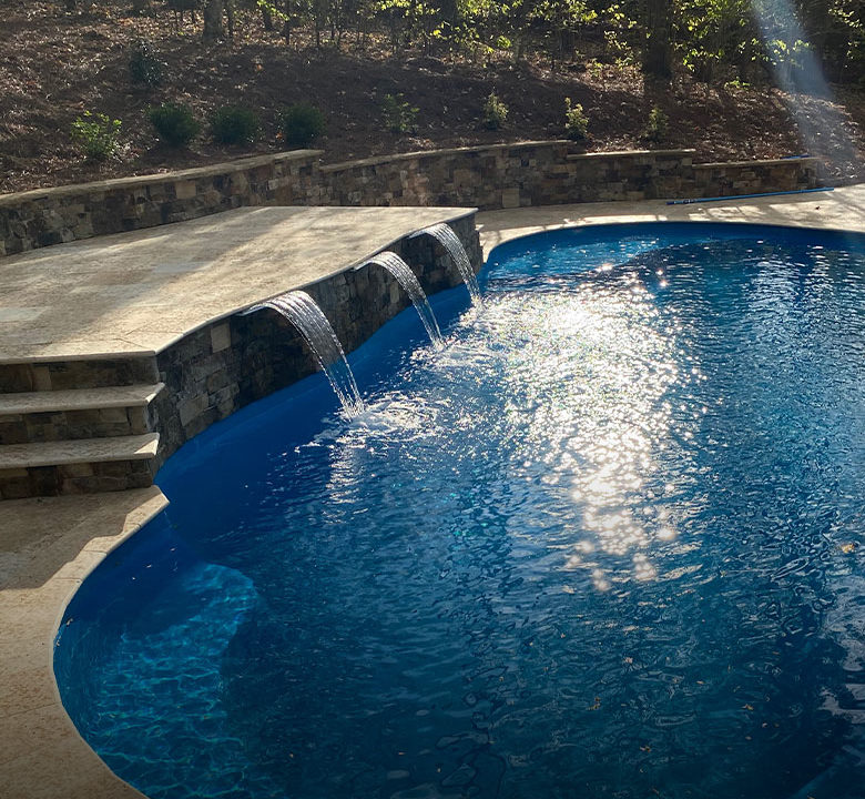 inground fiberglass pool with a waterfall ledge and retaining wall