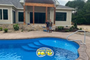 two people stand by an inground fiberglass pool with landscaping