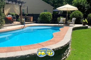 inground fiberglass pool with nice patio furniture and retaining ledge