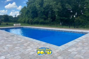 inground fiberglass pool with paver patio and black fencing